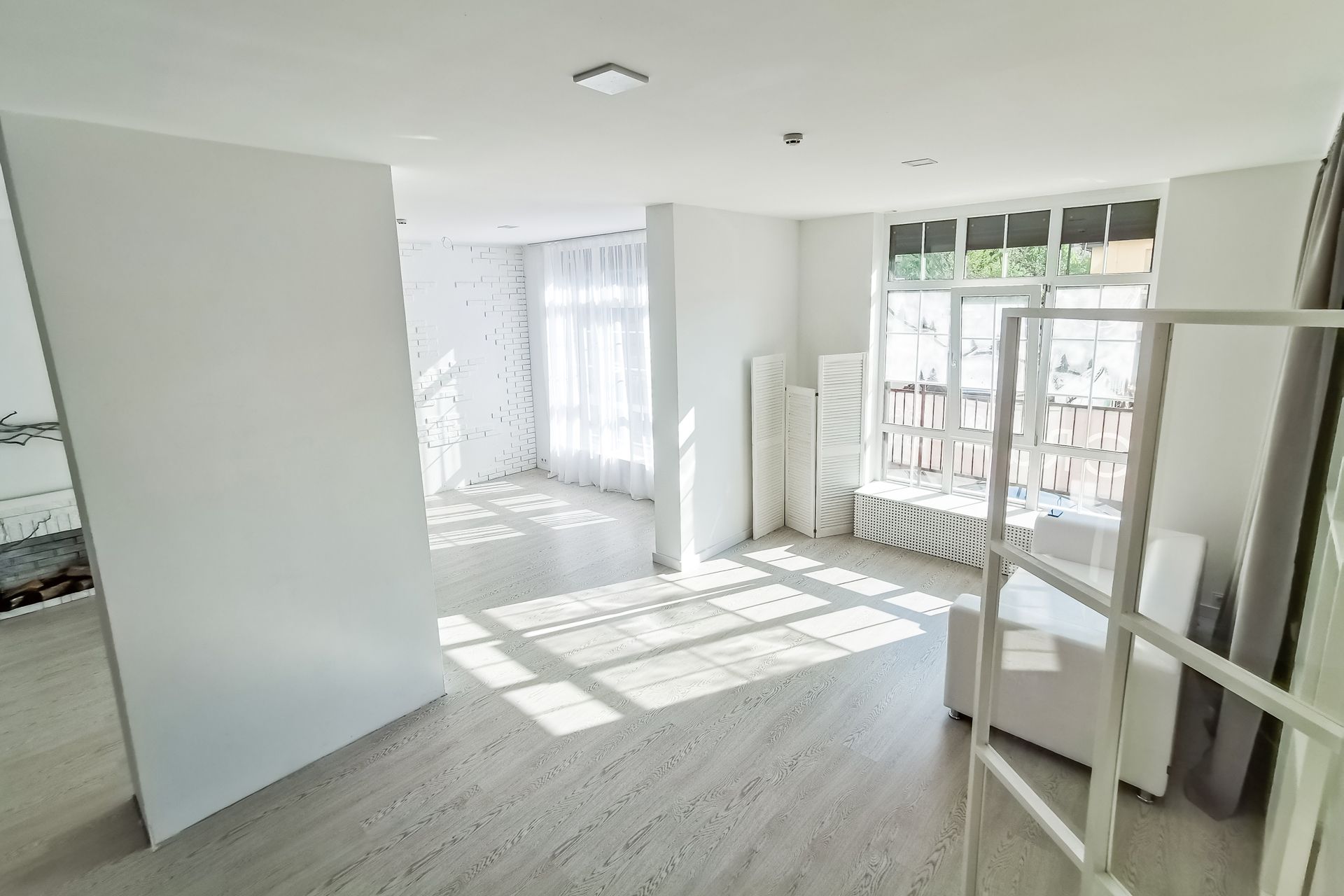 Bright white empty room with sunlight, large windows, curtains, and a metal shelf