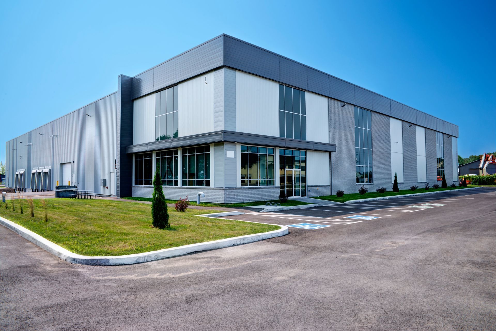 Modern gray industrial building with glass entrance, blue sky, and paved parking area