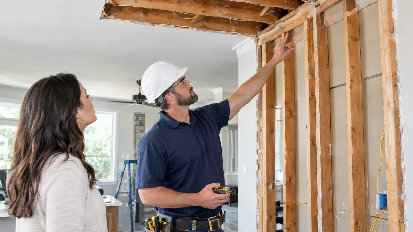 Contractor and homeowner examining exposed wooden wall framing and studs during remodel.