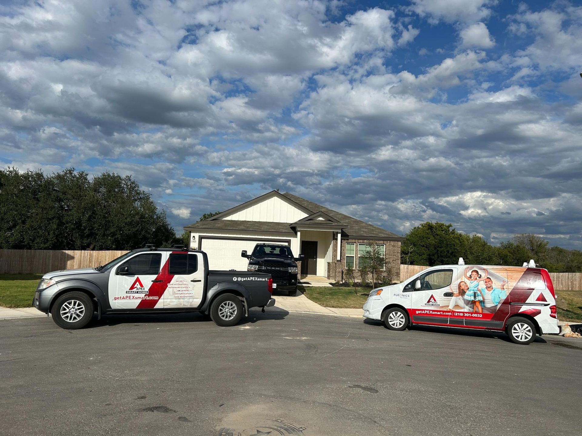 Two branded service trucks parked outside a small house under a cloudy sky.