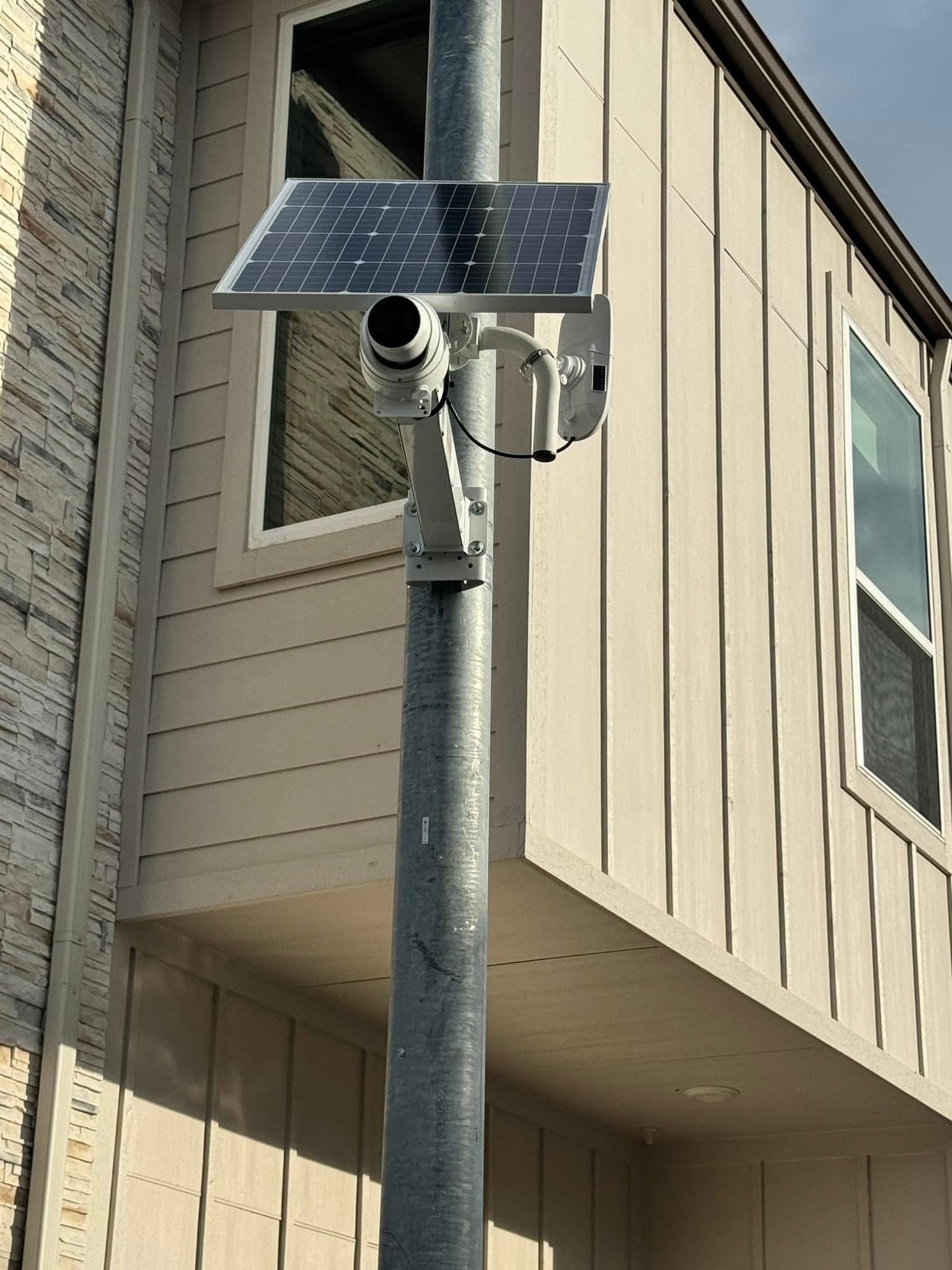 Solar-powered security camera mounted on a pole beside a beige building