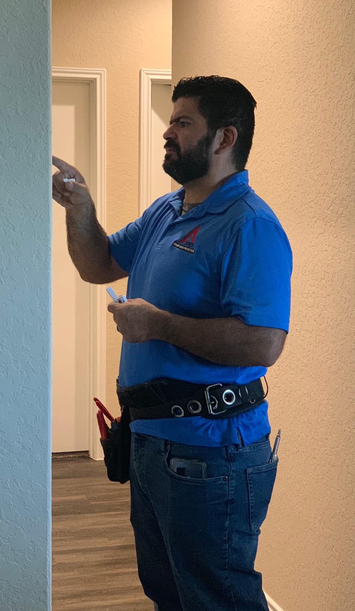 Man in blue polo shirt and jeans standing indoors, holding up a small object near a doorway.