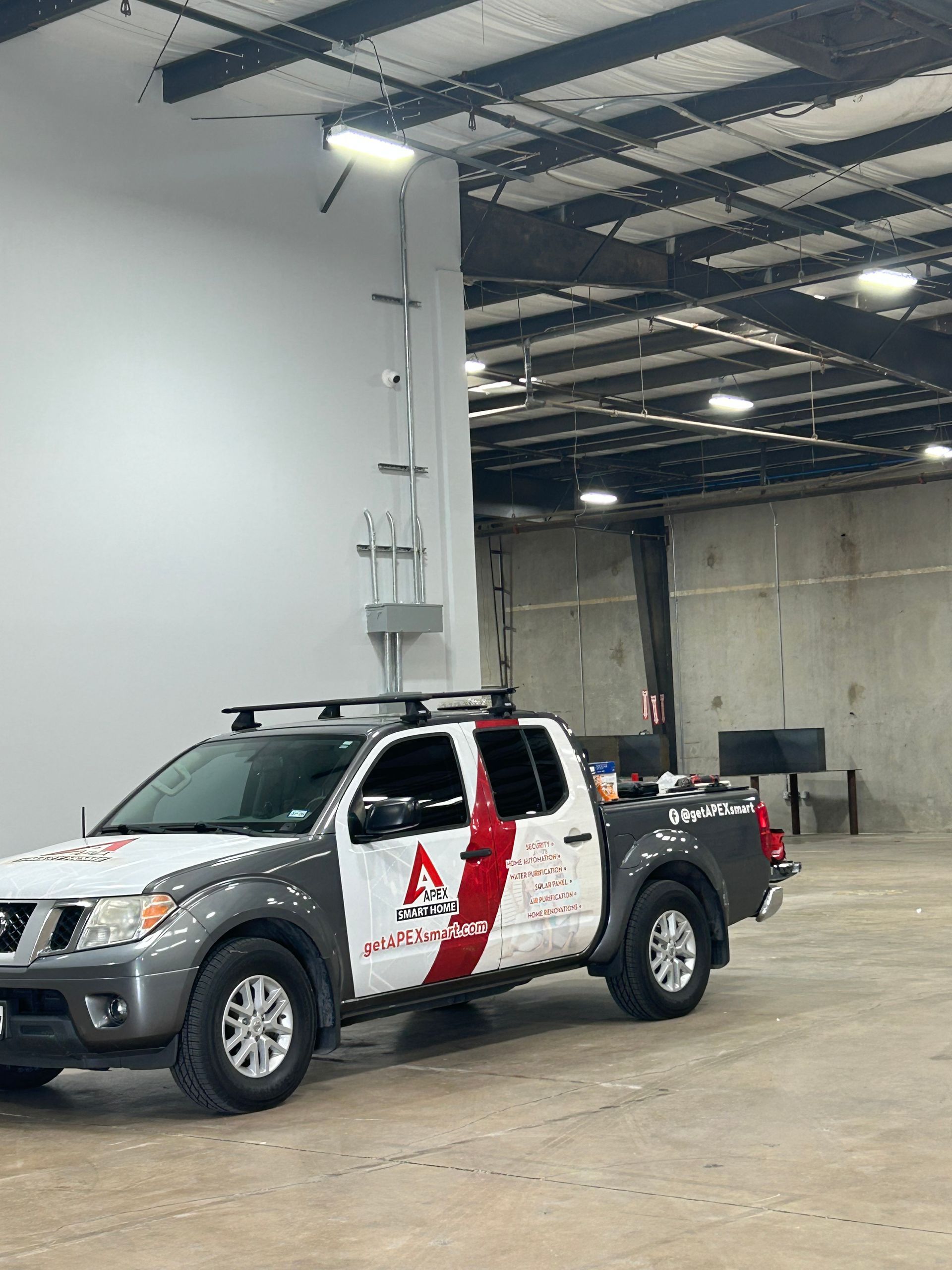 White utility truck with a roof-mounted light tower parked inside a warehouse.