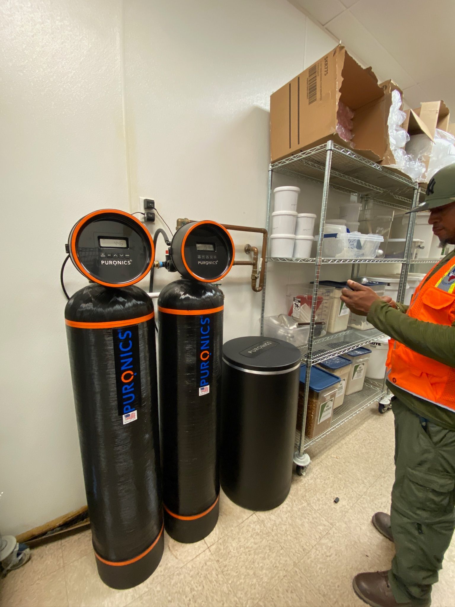 Two tall black cylinders with orange-rimmed tops beside metal shelving in a storage room.