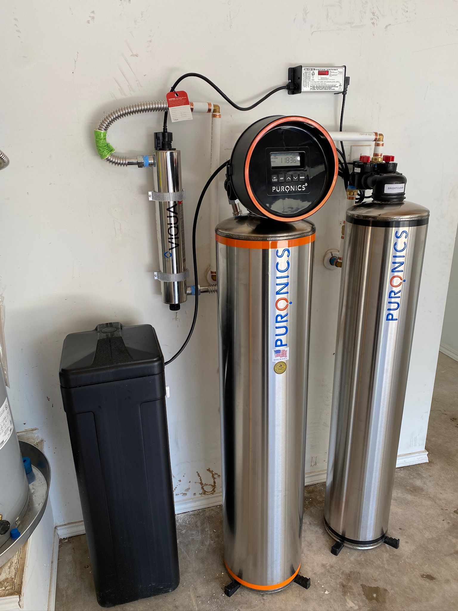 Water filtration system with three tall metal tanks and a black controller in a utility room.
