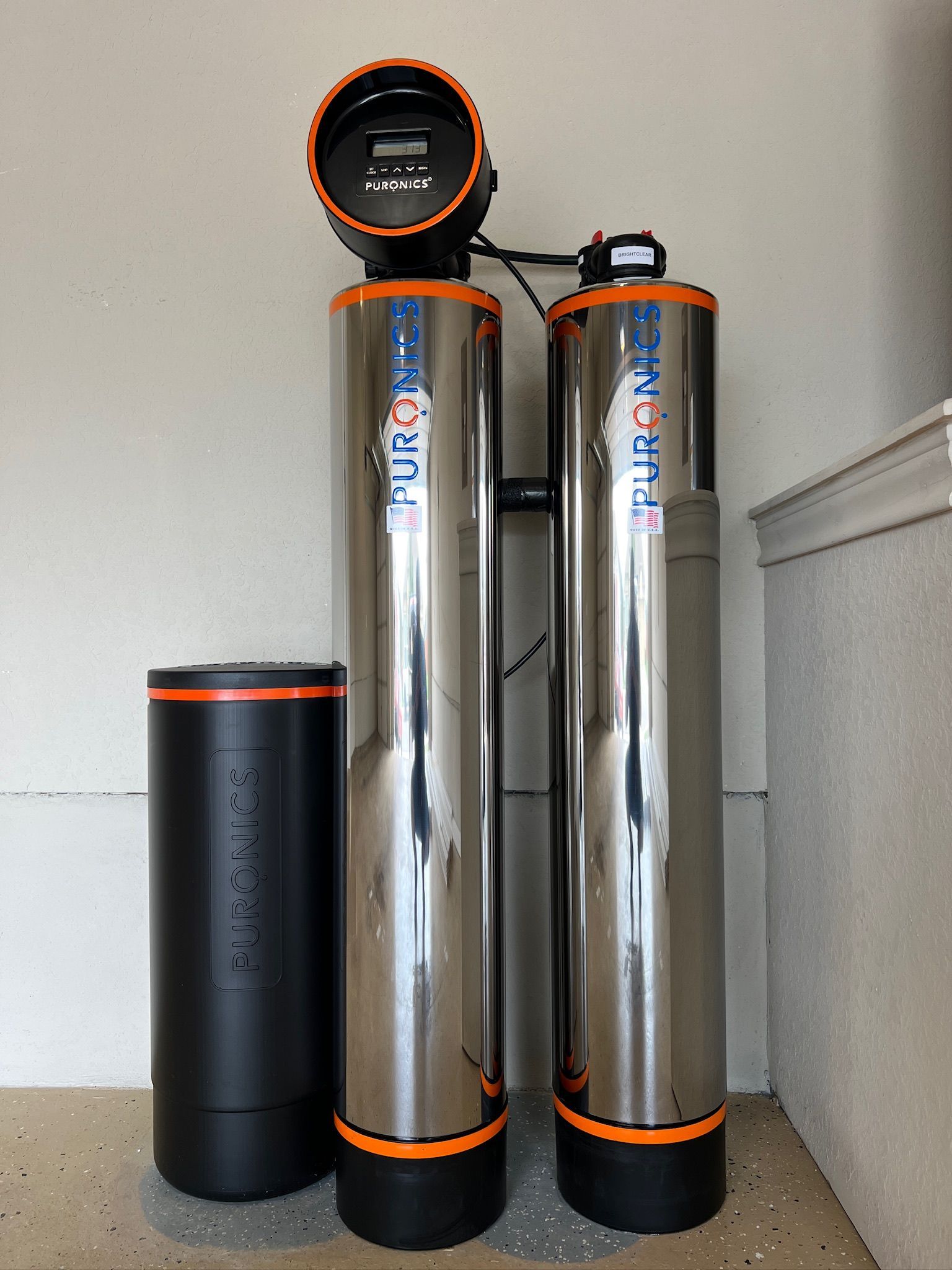 Three tall silver-and-black cylinders with orange accents standing beside a black bin indoors