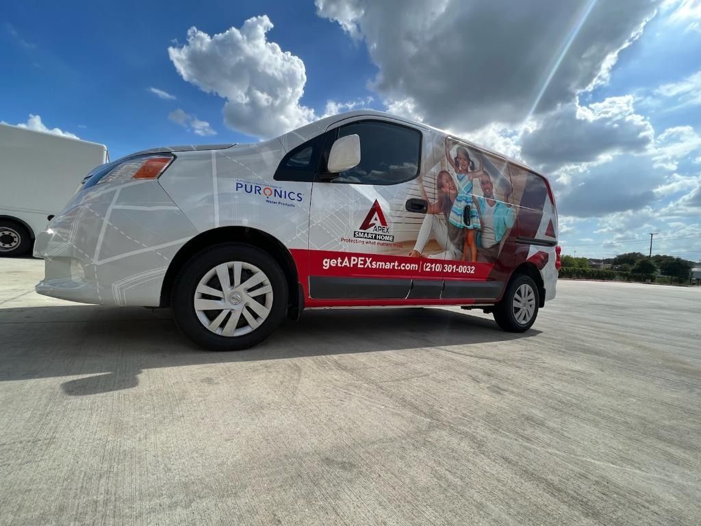 White wrapped sedan with red graphics parked on pavement under a blue sky with clouds