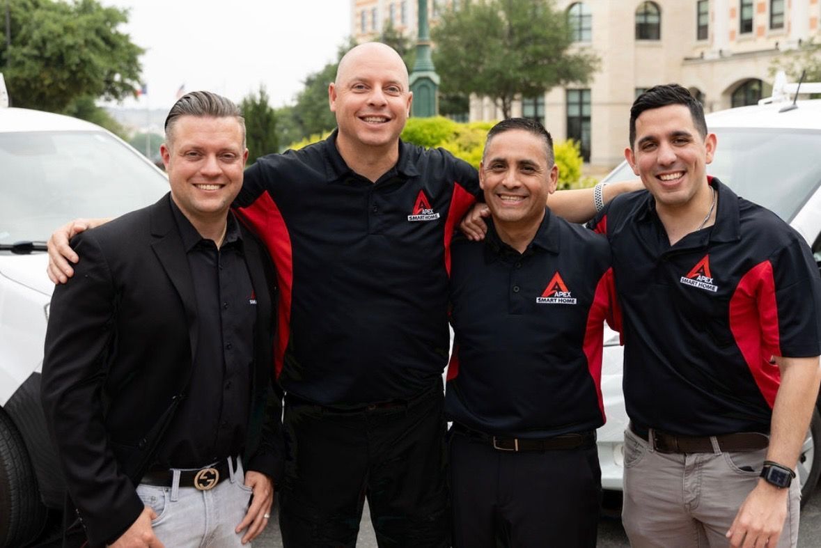 Four coworkers in black and red shirts smiling outdoors, standing arm in arm