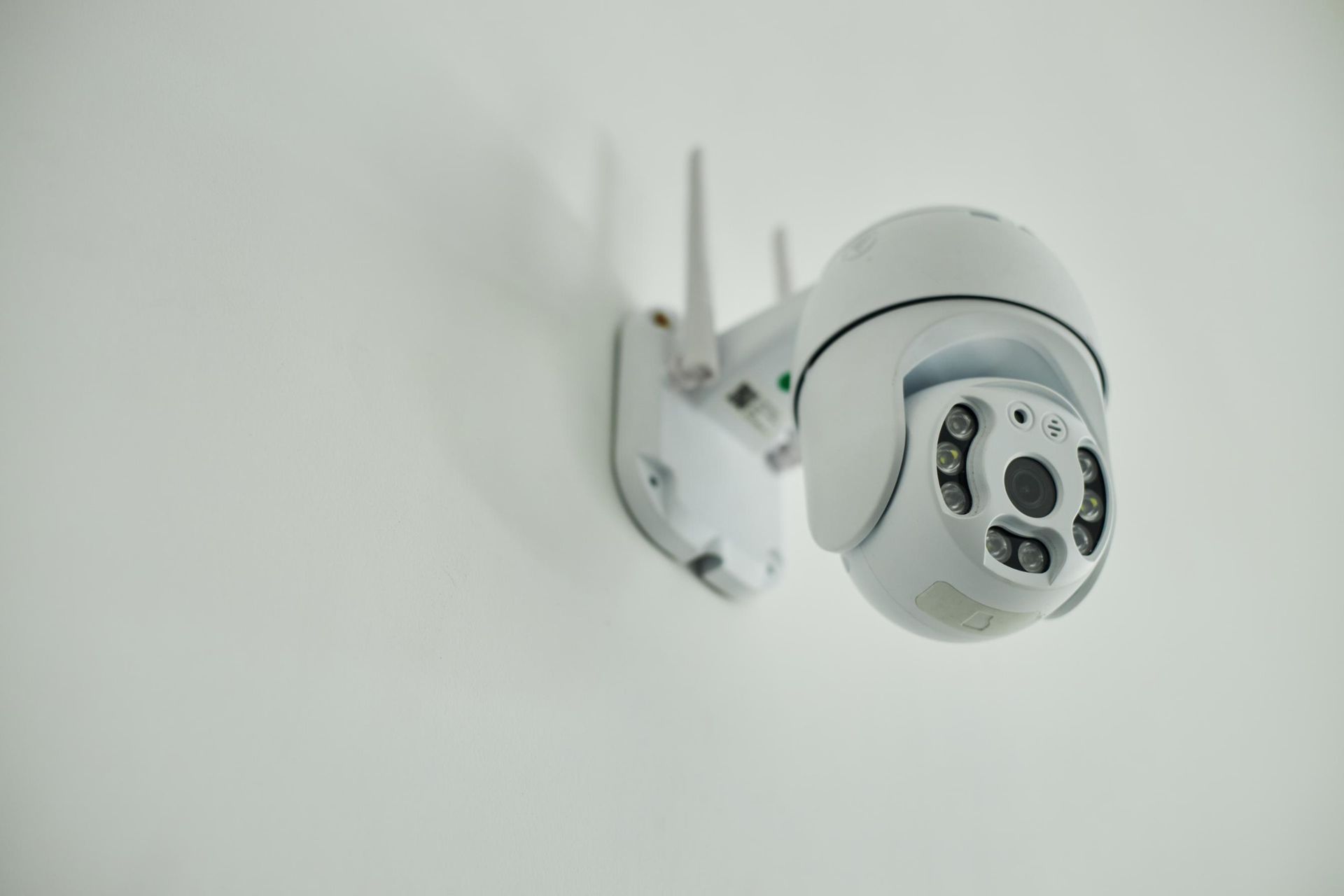 White security camera mounted on a wall, angled downward with a visible lens and antennae