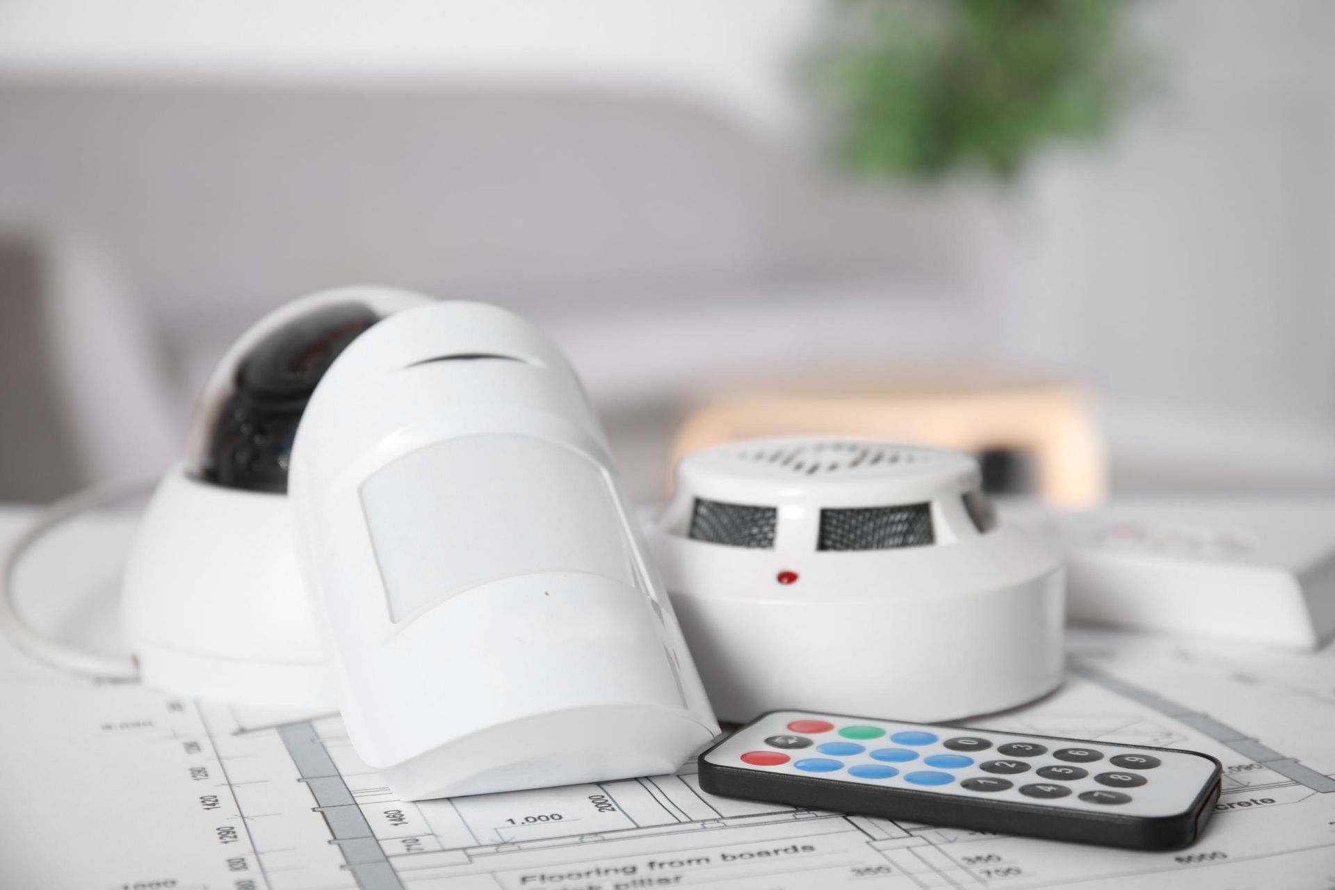 White home security camera, motion sensor, and remote control on a desk with paperwork