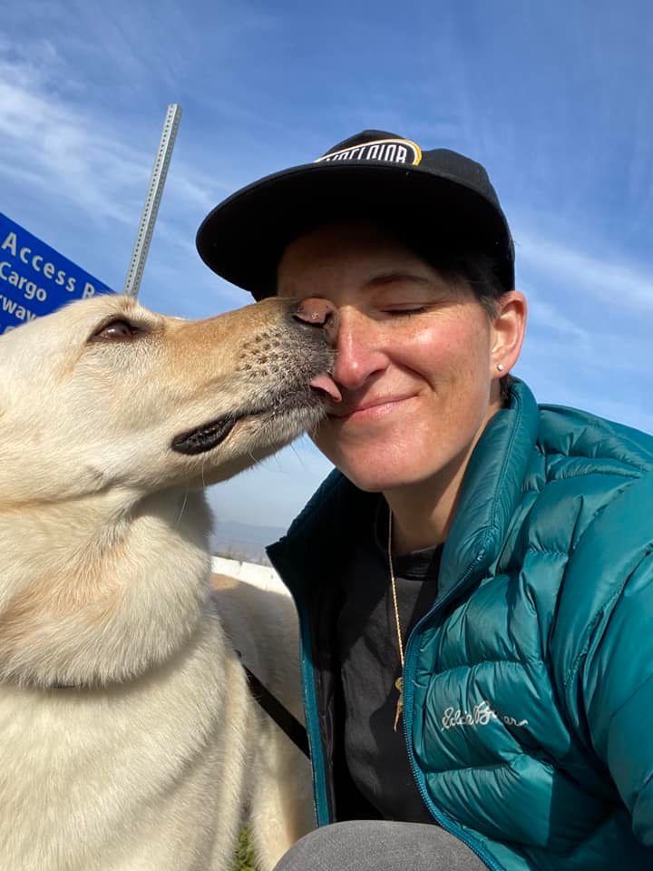 A woman in a green jacket is kissing a dog on the nose