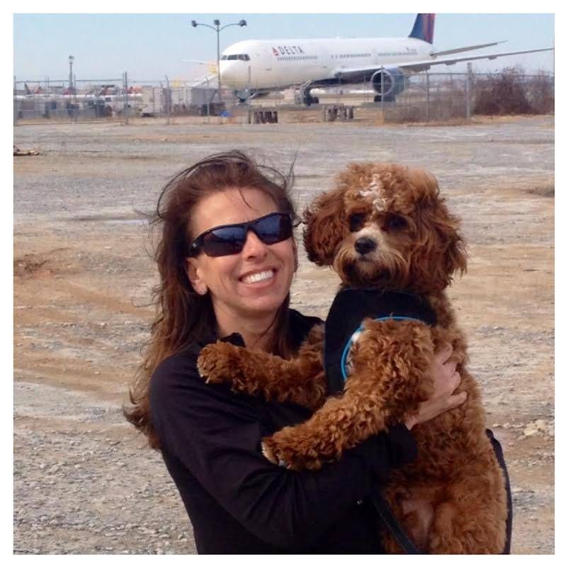 A woman is holding a dog in front of a delta airplane