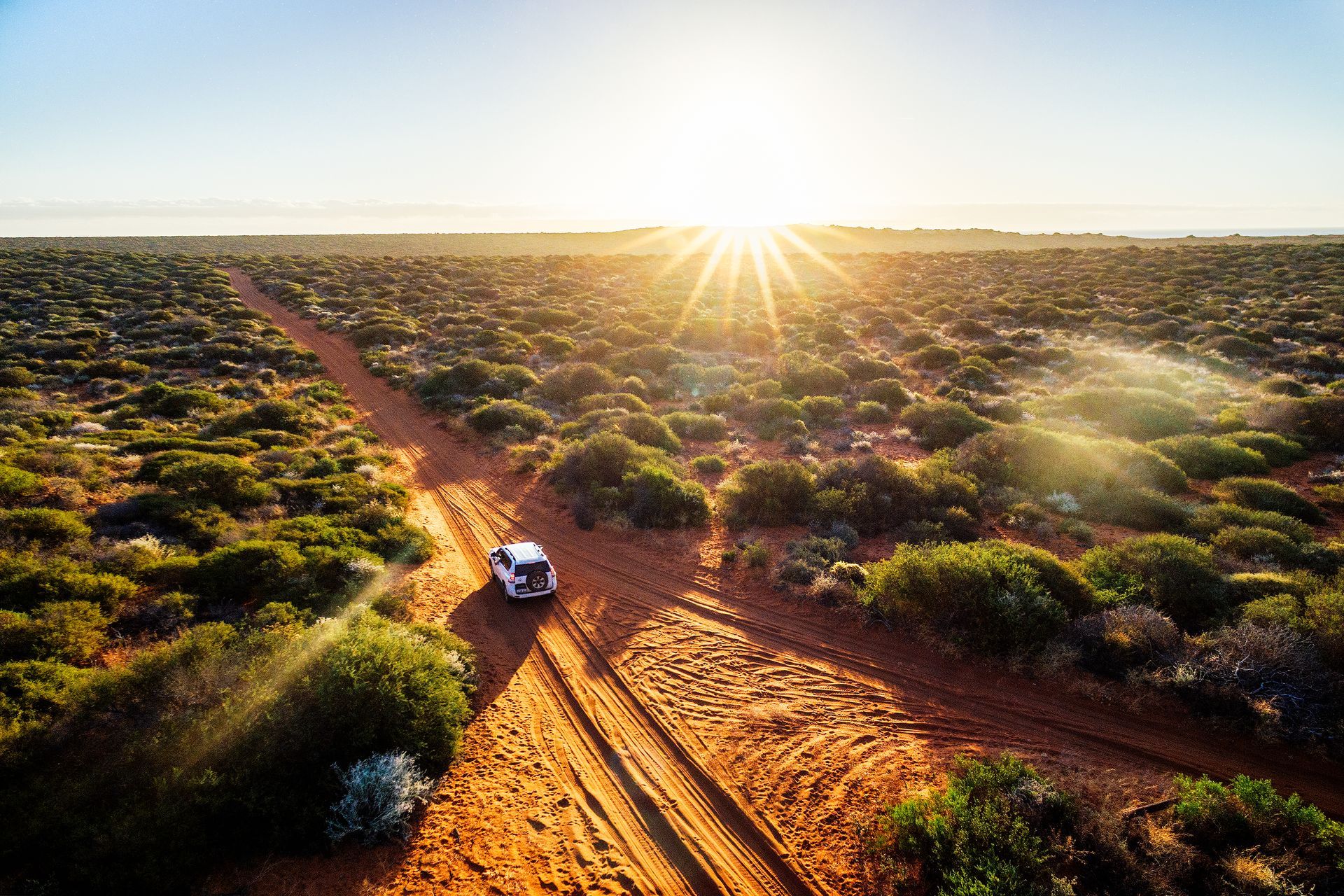 An aerial view of a car driving down a dirt road in the desert.