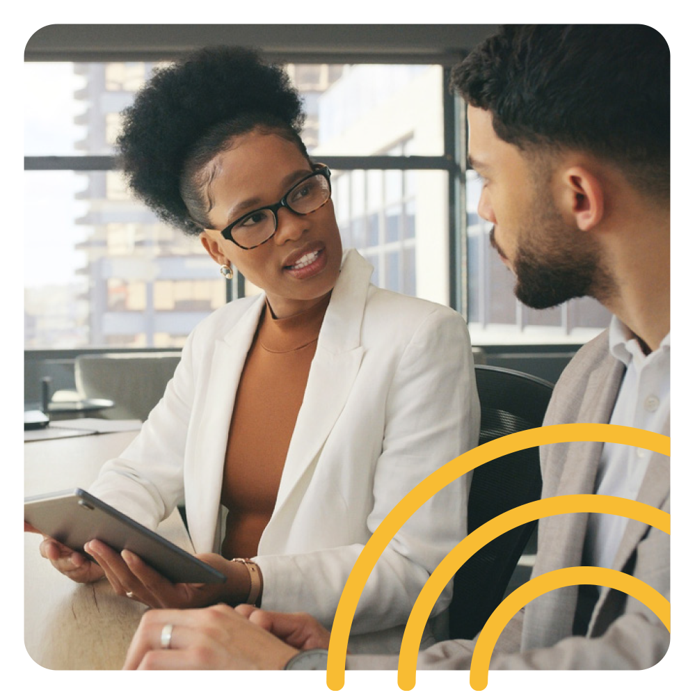 a woman is sitting at a table talking to a man while holding a tablet .