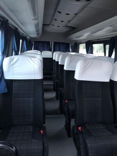 Interior vacío de un autobús con filas de asientos negros y fundas blancas para los reposacabezas.