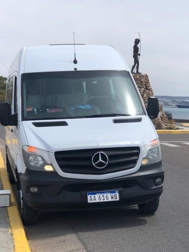 Una furgoneta Mercedes Sprinter blanca aparcada en una carretera, con una persona de pie sobre unas rocas junto al mar.