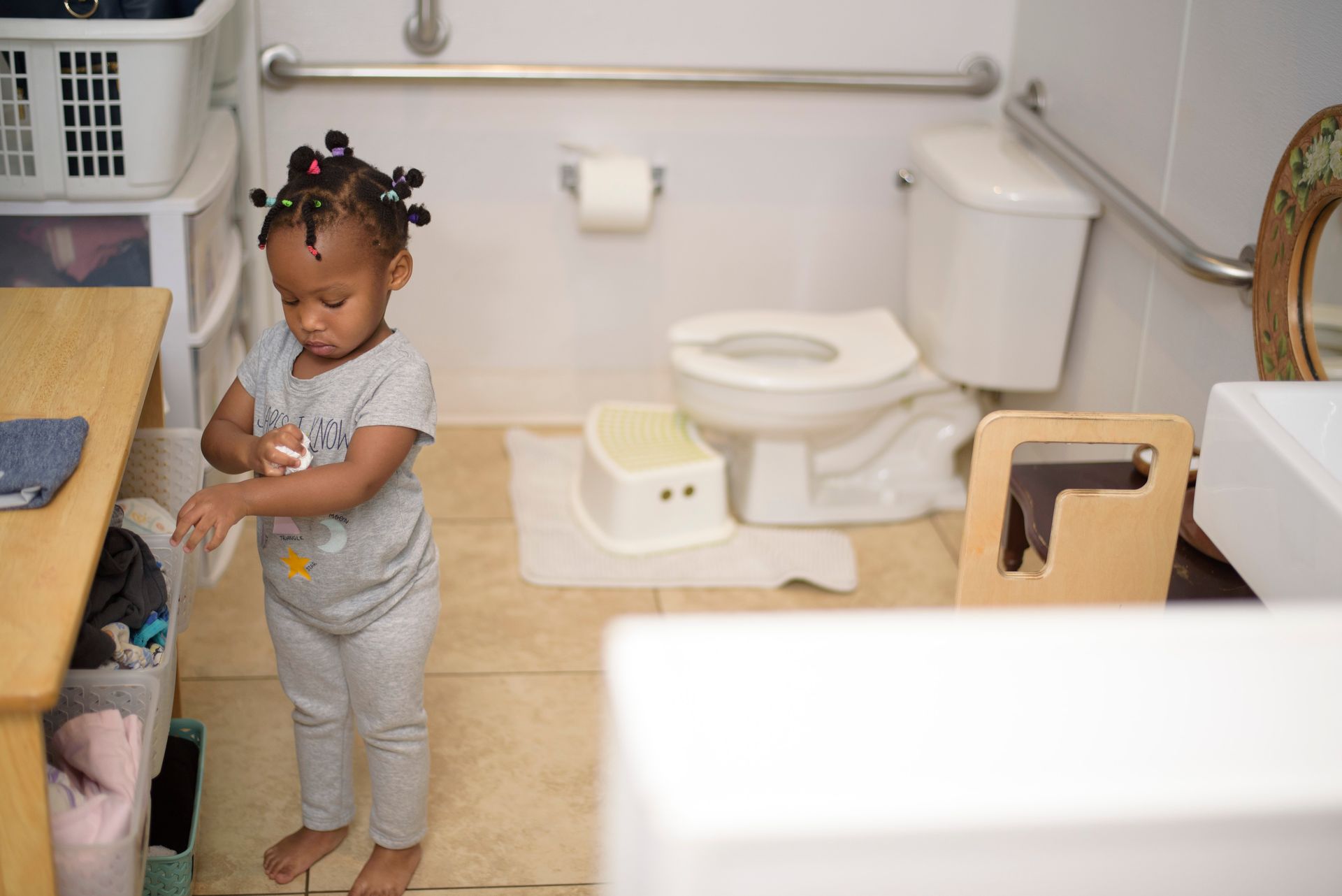 Toddler standing in a bathroom beside a sink and toilet, drying hands.