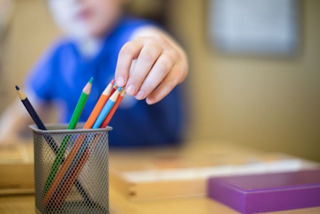 Child reaching for colored pencils in a classroom setting