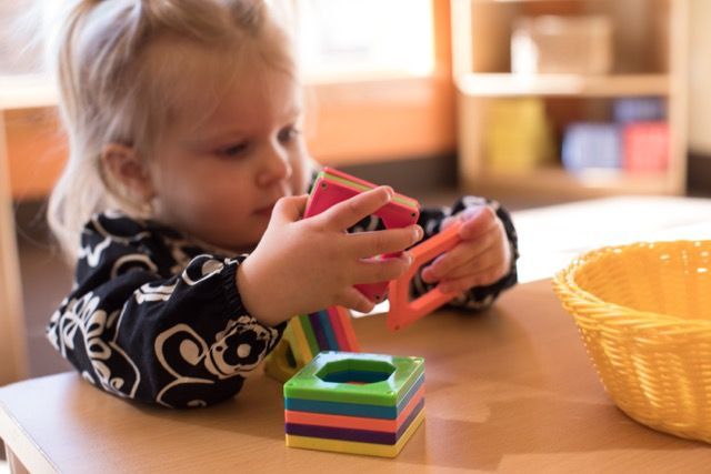 Child stacking colorful blocks at a table beside a yellow basket