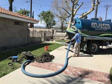 Worker pumping sludge from a tanker truck into a hose in a residential driveway.