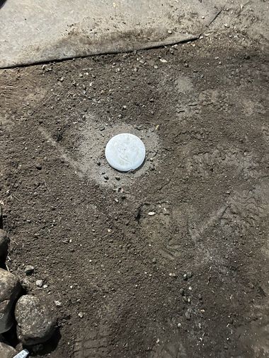 White circular cap embedded in dirt beside a concrete edge.