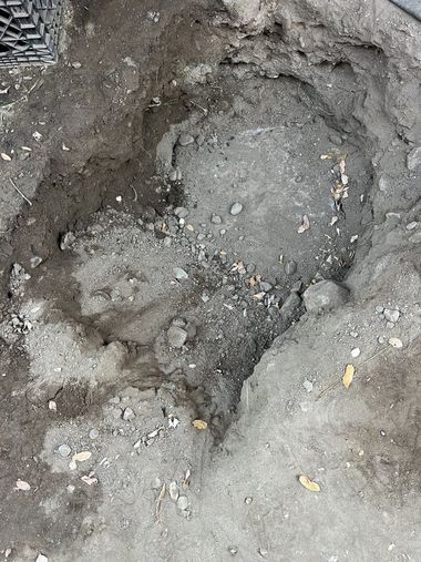 Close-up of a muddy hole in the ground with loose rocks and dirt