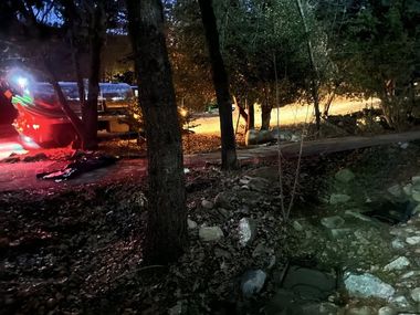 Nighttime scene with red-lit emergency vehicle on a wooded roadside near a rocky stream
