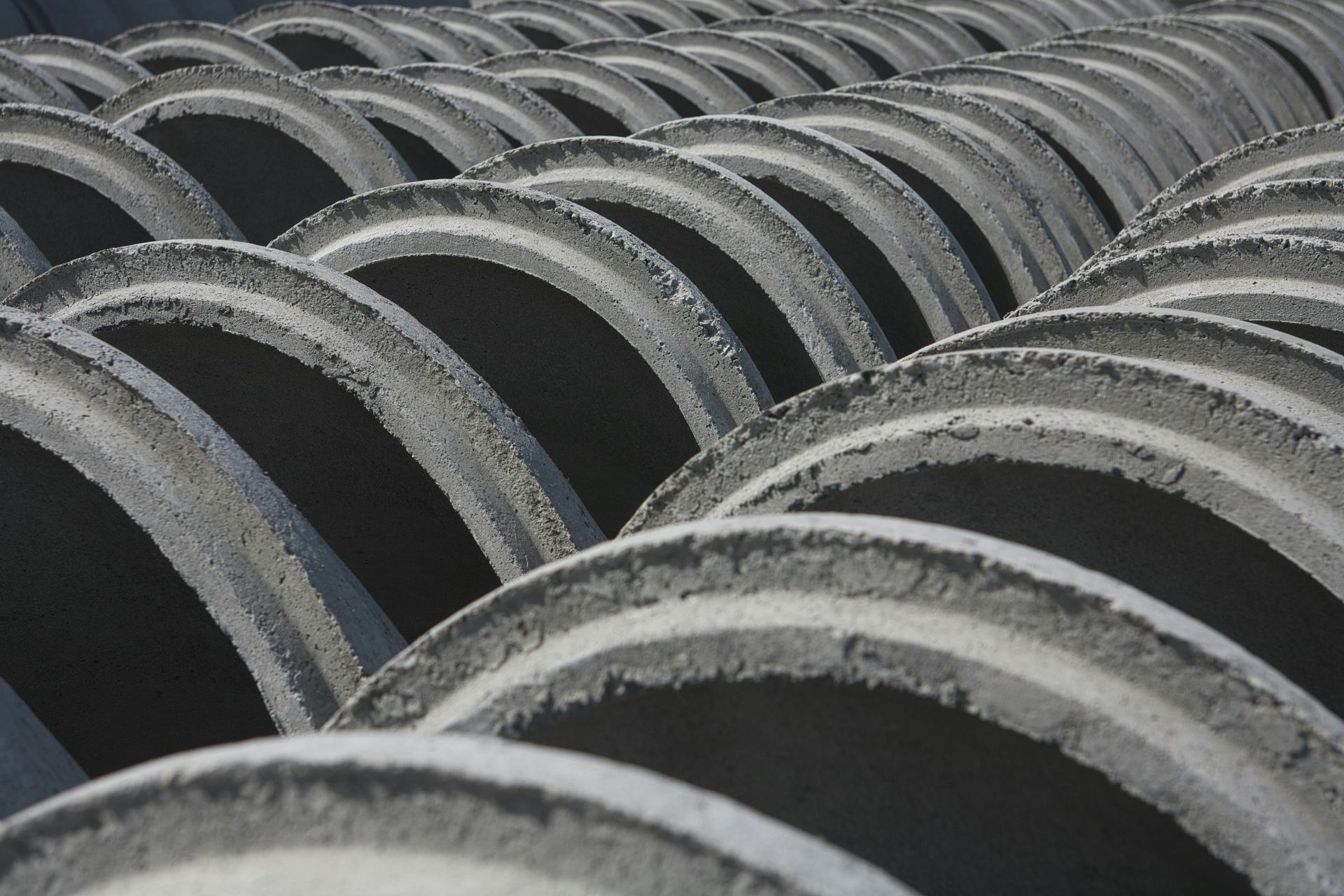 Rows of large concrete pipes stacked in an industrial setting, creating repeating gray arches
