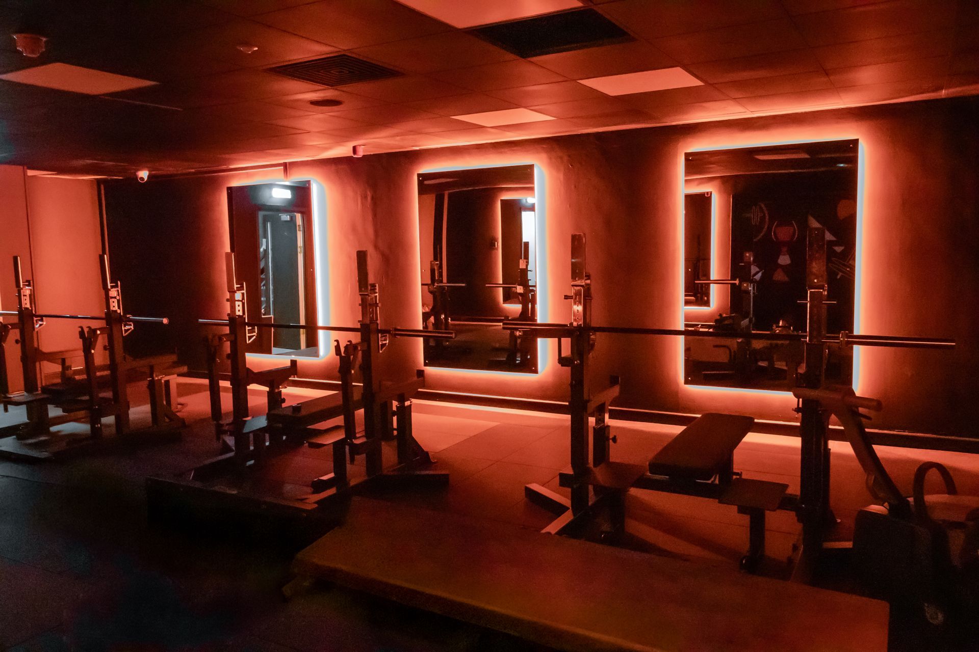 Squat racks and lit mirrors in the strength area at Fervid Fitness