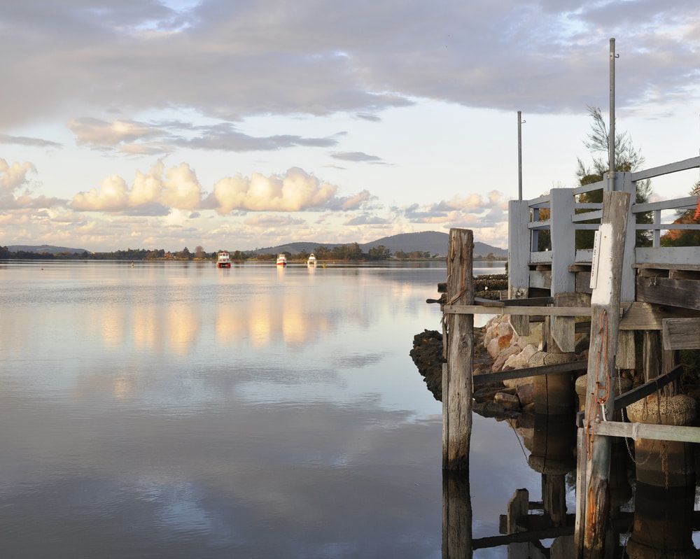 A Dock Overlooking a Body of Water with Mountains in The Background — Brookes Engraving & Signs in Nowra, NSW