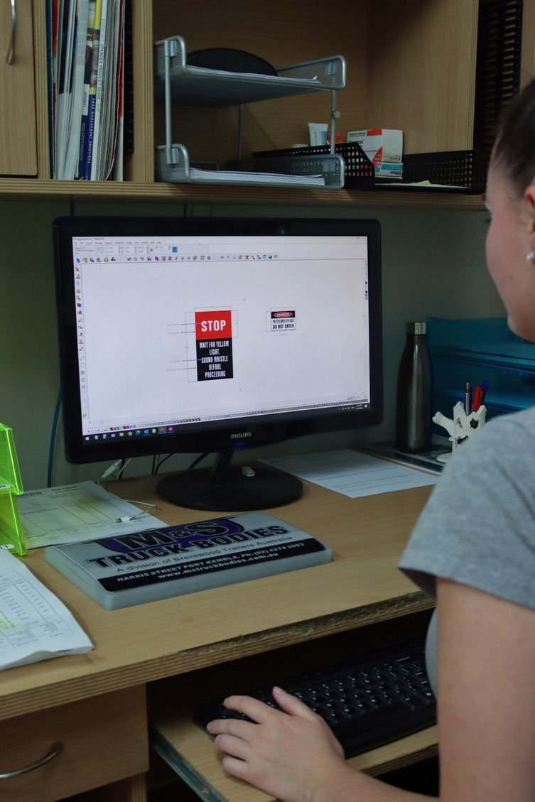 A woman sits at a desk using a computer with a stop sign on the screen — Brookes Engraving & Signs in Woonona, NSW