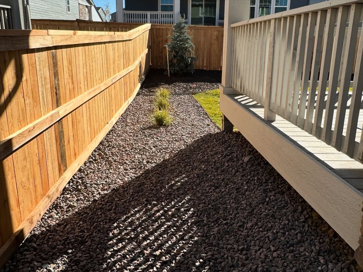 A narrow backyard side yard featuring dark gravel ground cover, a wooden privacy fence, and an elevated wooden deck.