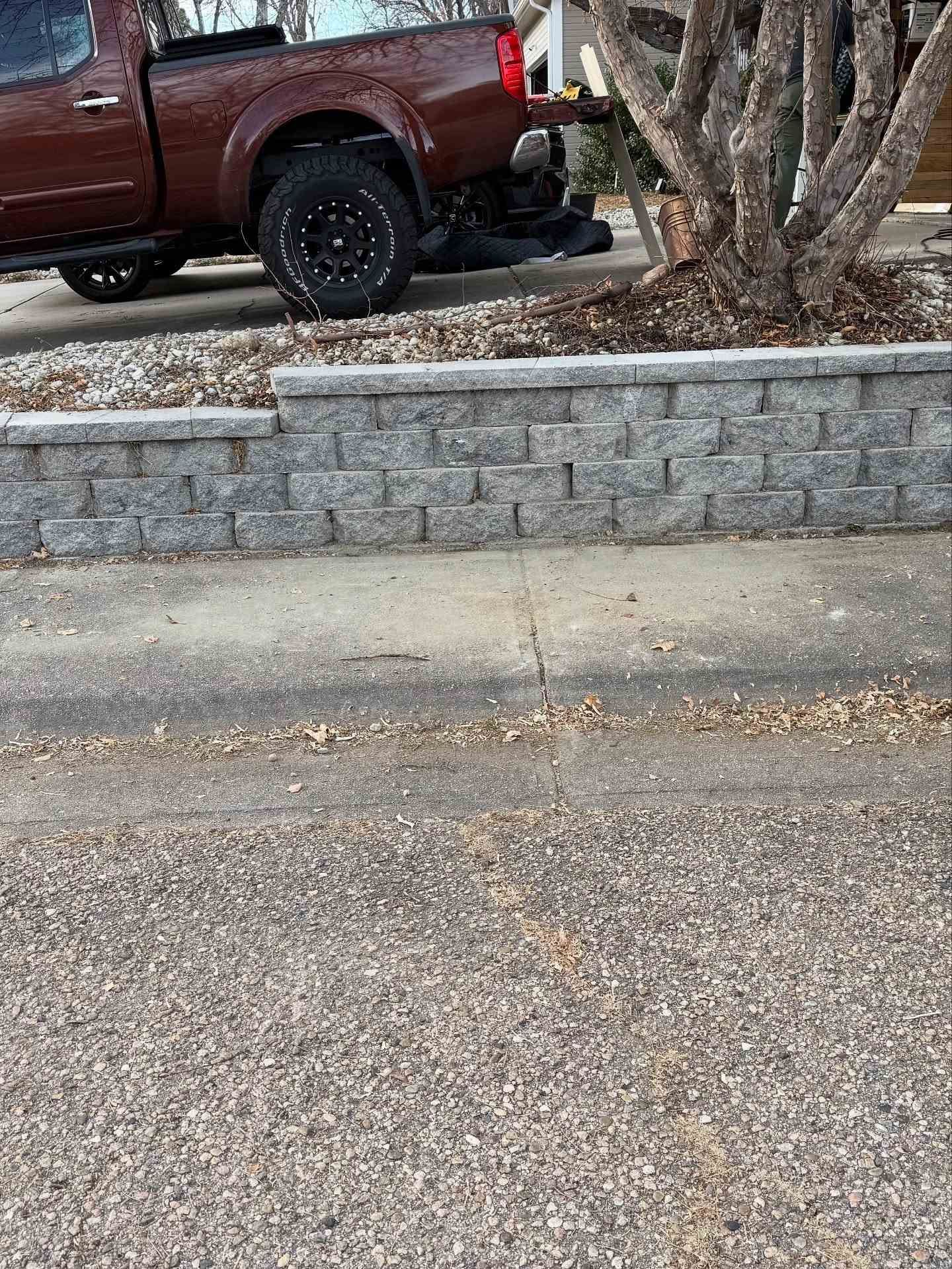 A dark red pickup truck parked on a driveway behind a decorative gray stone retaining wall.