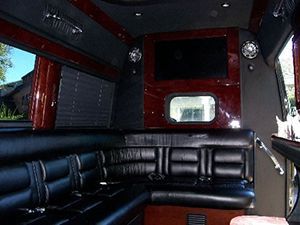 The inside of a limousine with black leather seats and a flat screen tv.