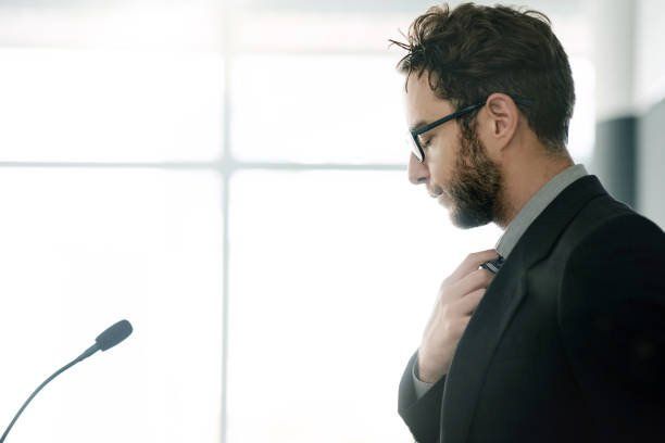 a man in a suit and tie is adjusting his tie in front of a microphone .