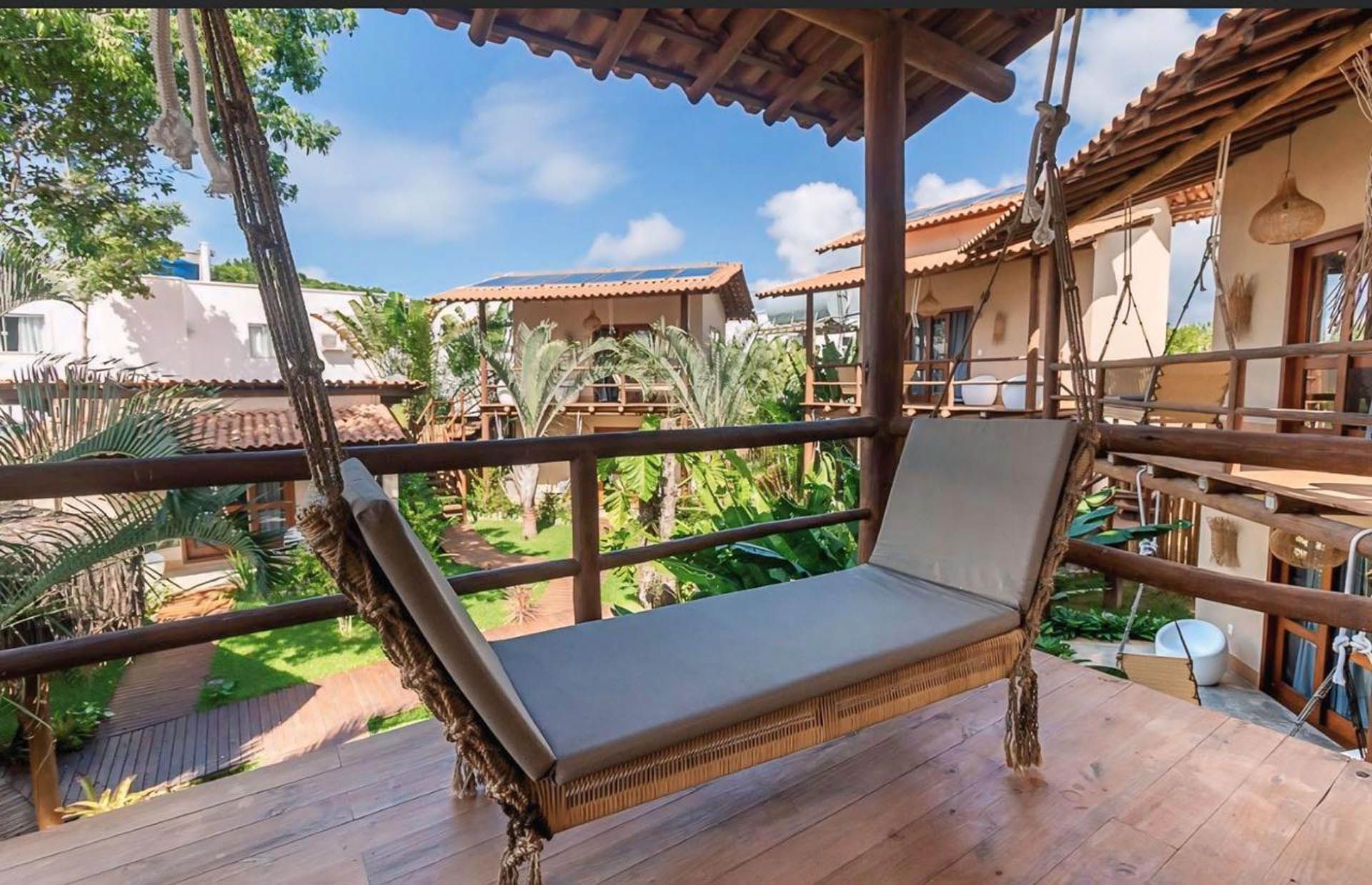 Sala de estar com varanda de madeira e divã almofadado com vista para um exuberante pátio tropical.