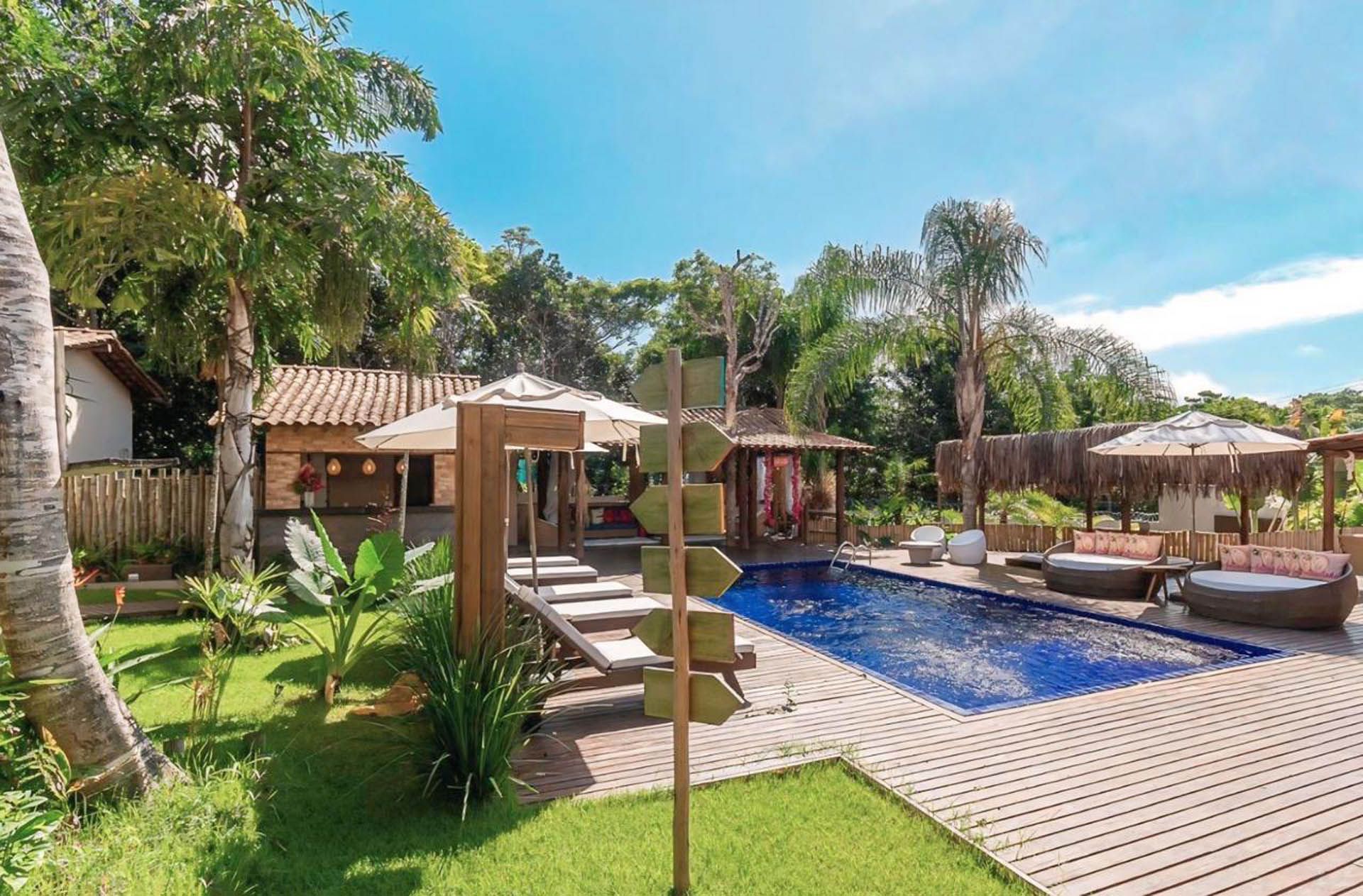 Piscina de luxo no quintal com água azul, cabanas, palmeiras e espreguiçadeiras sob um céu radiante.