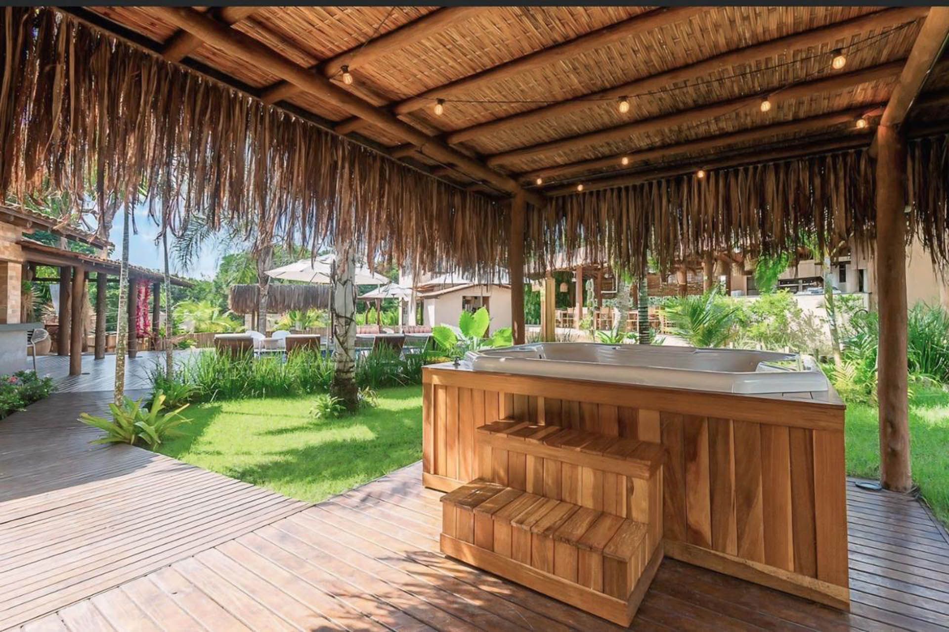 Bar de bambu ao ar livre sob um telhado de palha, com vista para um jardim tropical verdejante.