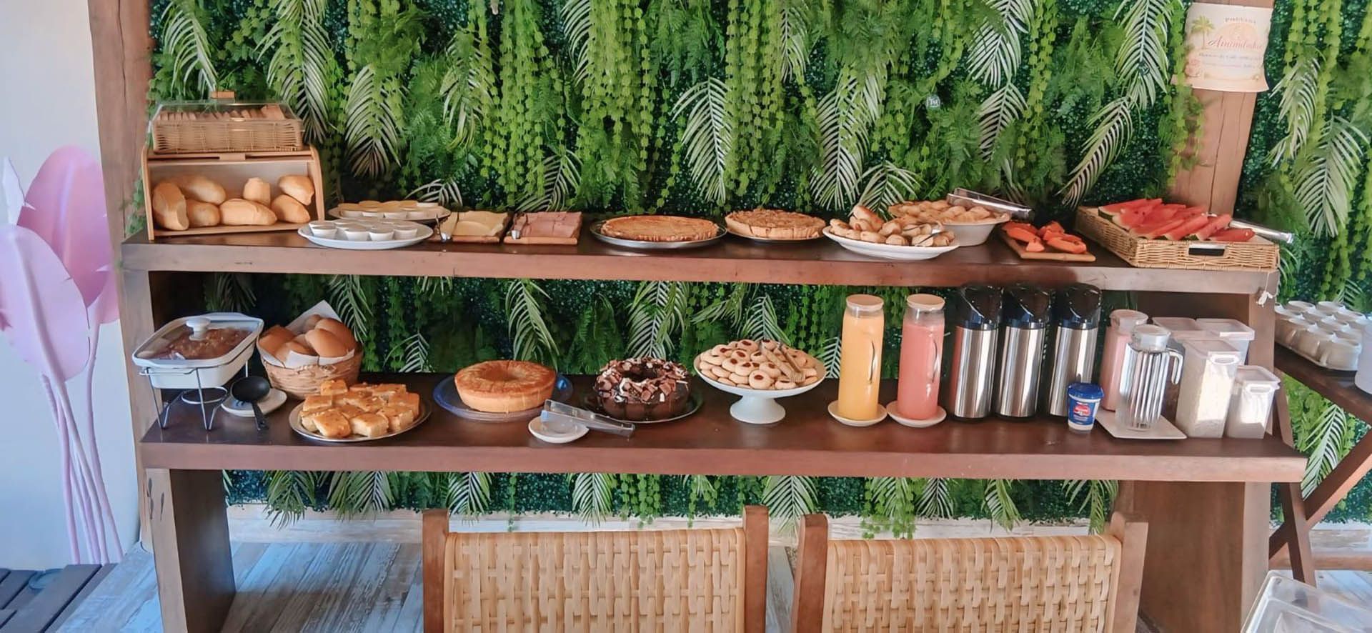 Mesa rústica com tigelas, potes e bandejas de petiscos em um fundo de plantas verdes.