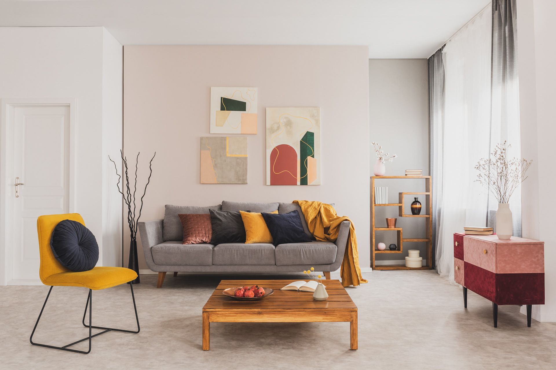 A living room with a couch , chair , coffee table and paintings on the wall.