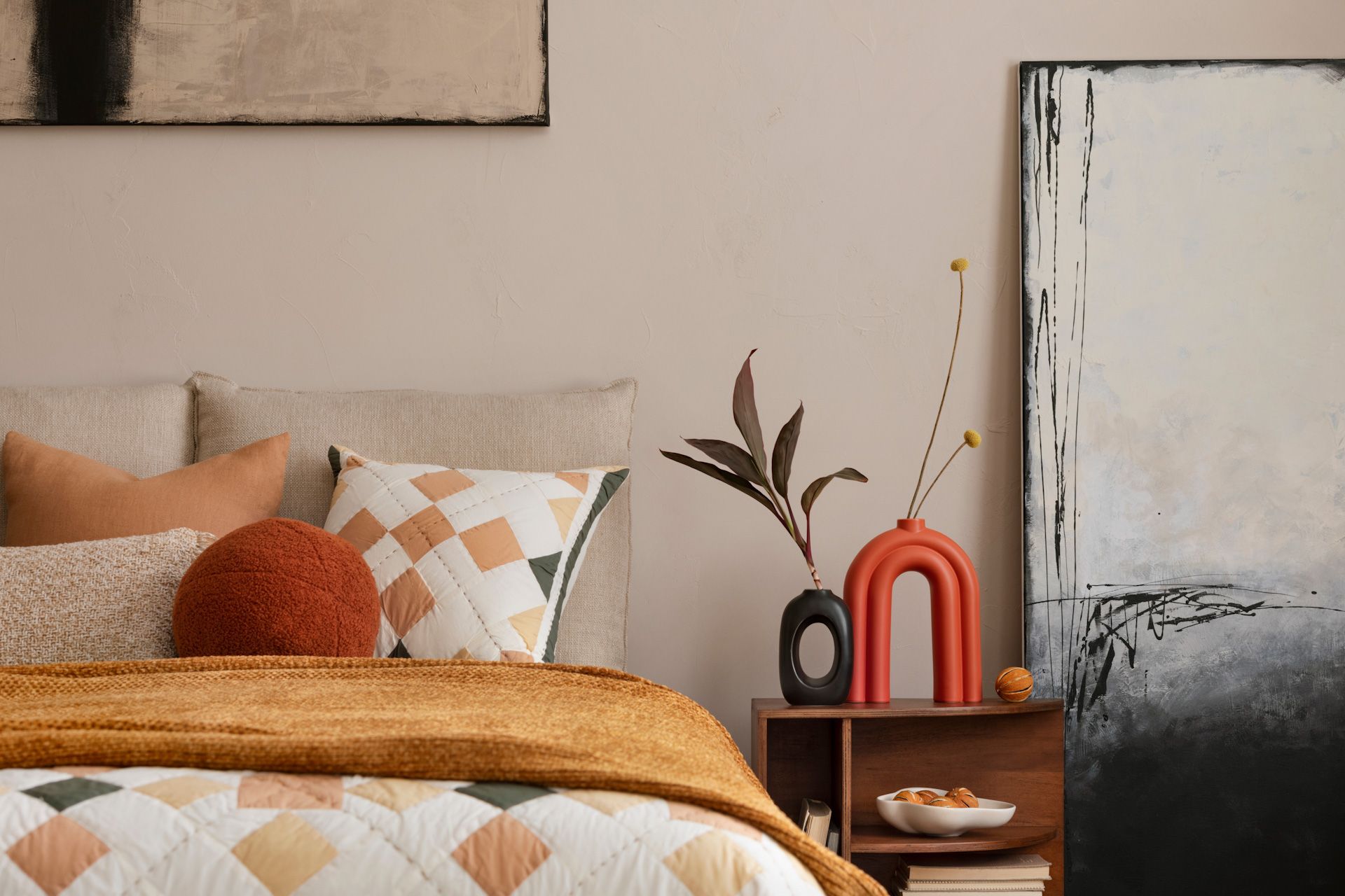 A bedroom with a bed , nightstand , vases and paintings on the wall.