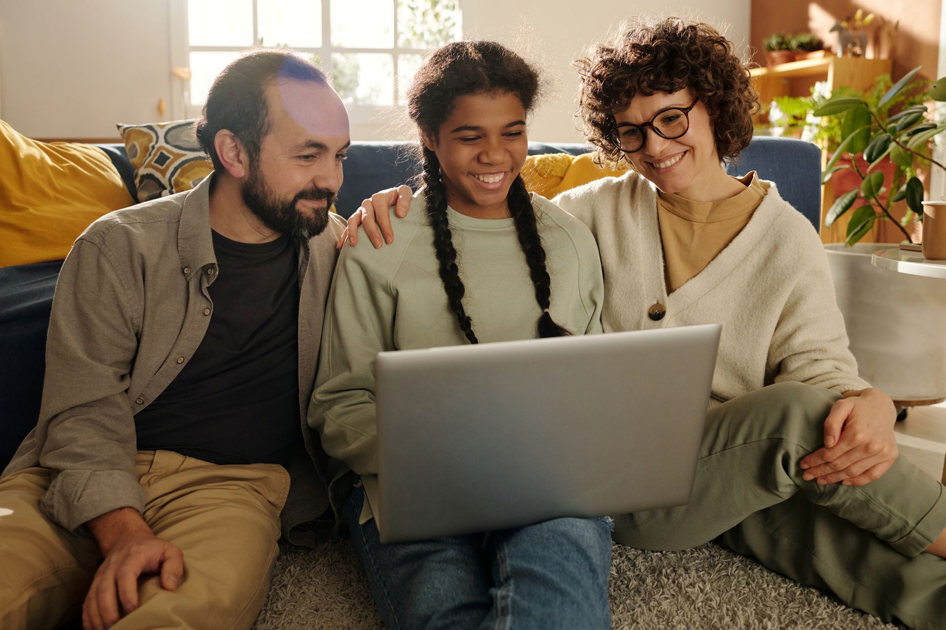Family of three, a father, daughter, and mother, looking at a laptop together indoors.