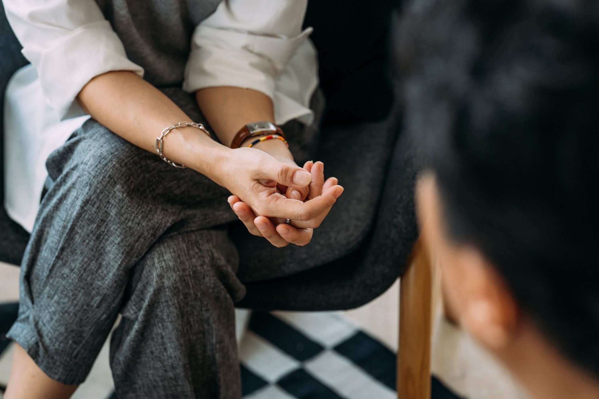 Woman in therapy session, hands clasped, speaking to unseen person.