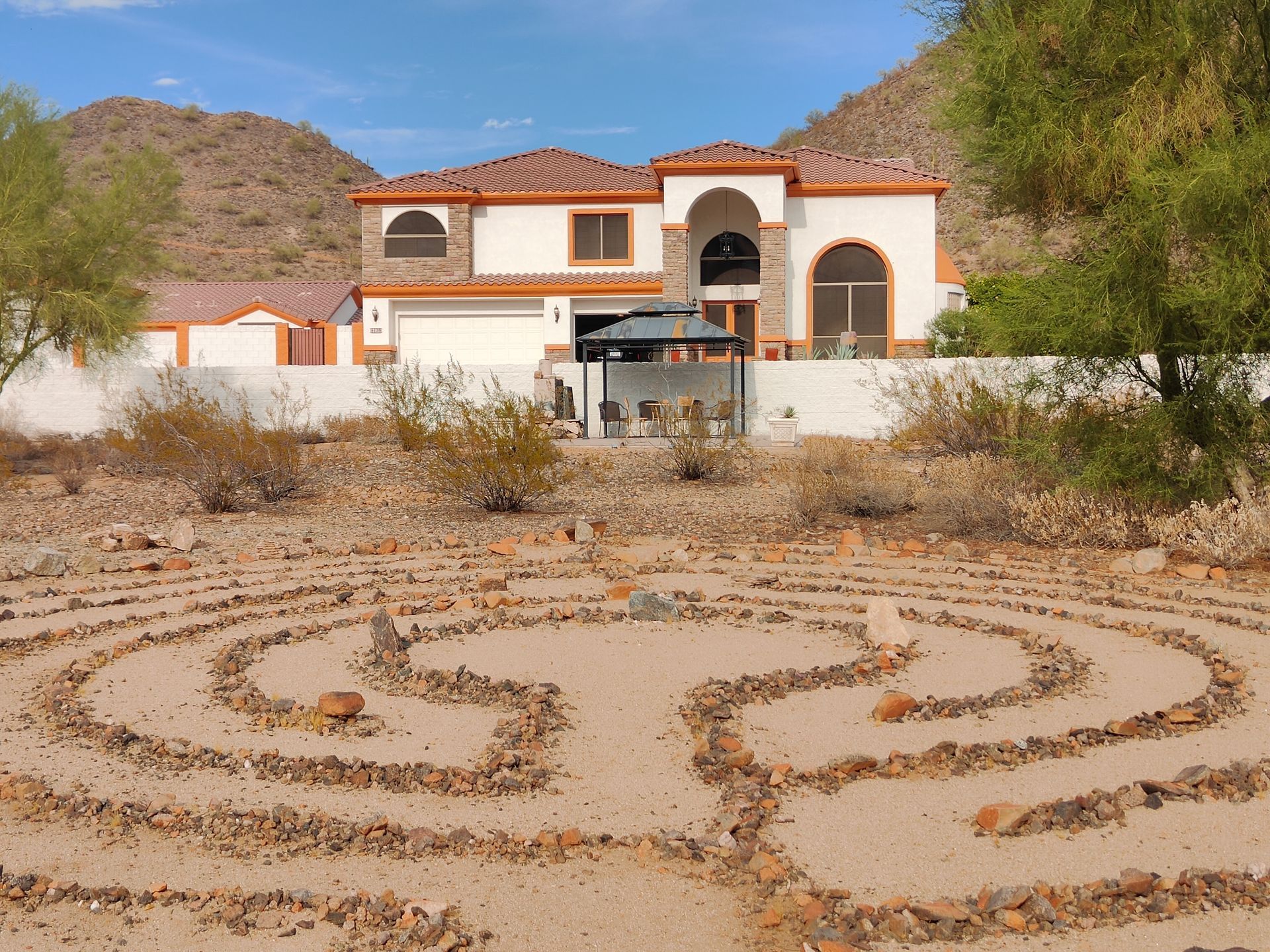 A wooden bench sits in front of a labyrinth with a house in the background.