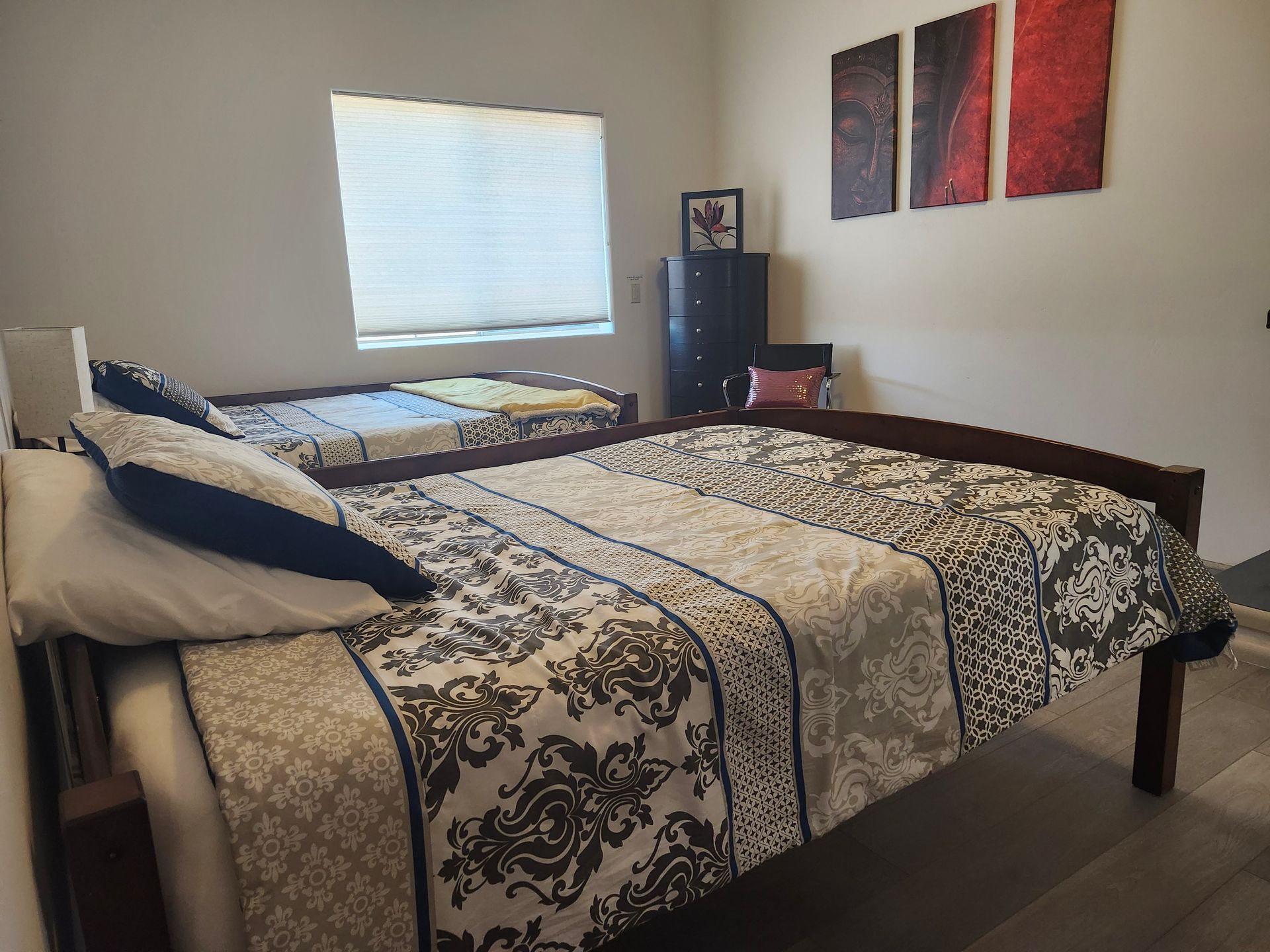 Bedroom with a neatly made bed, patterned quilt, window, and wall art.