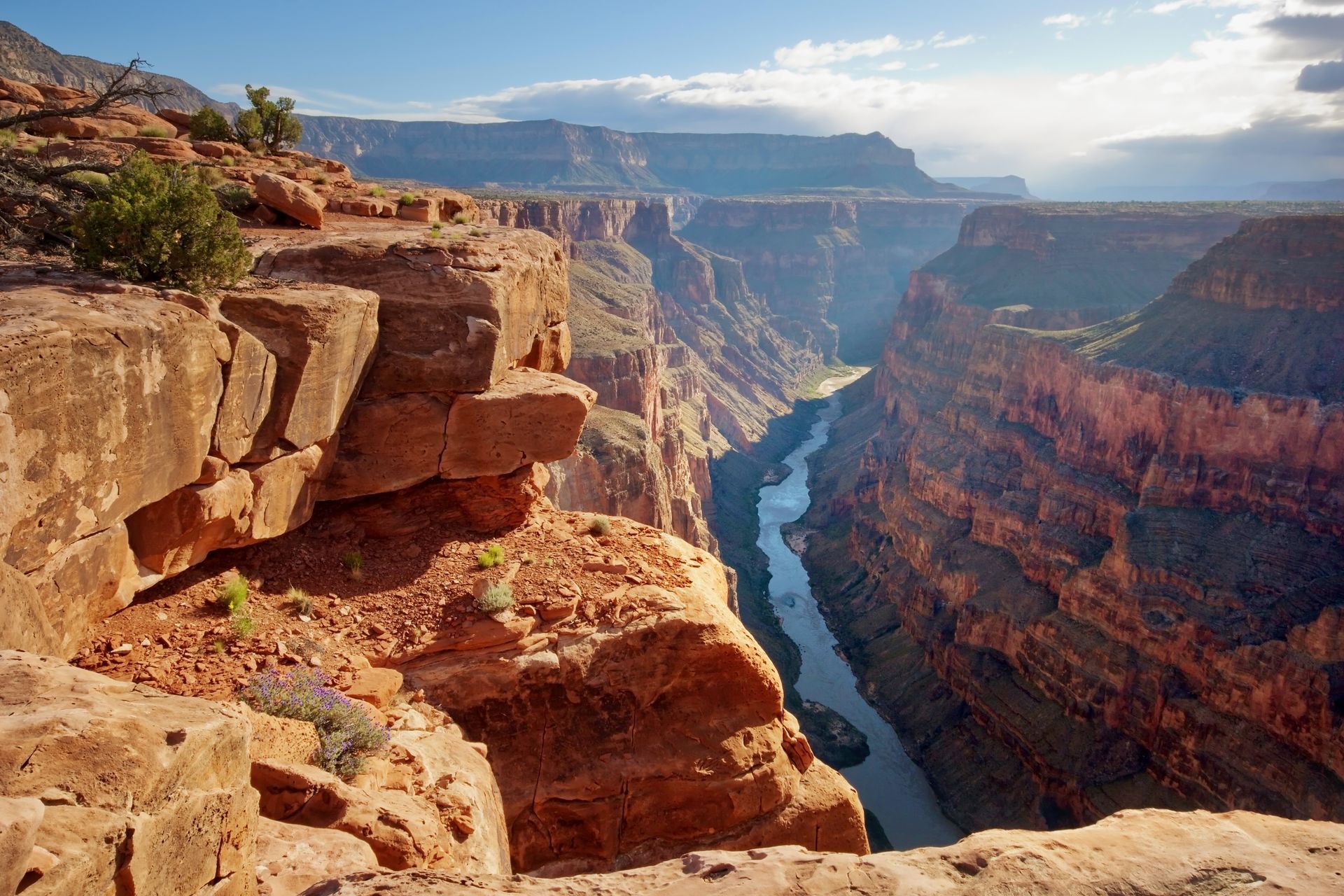 Grand Canyon overlook with layered red cliffs and a river winding through the gorge under a bright sky