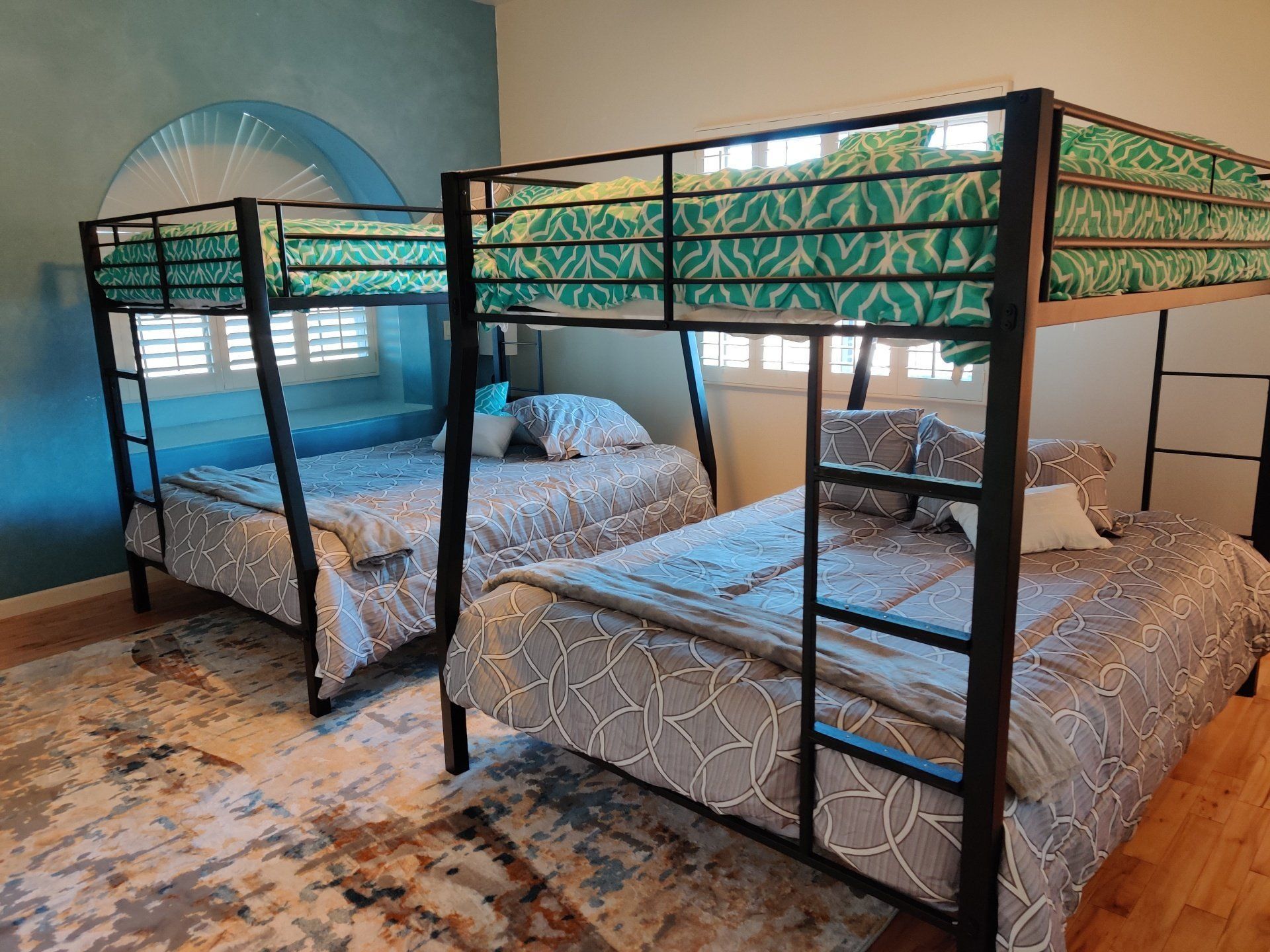 Two metal bunk beds with patterned bedding in a small bedroom with teal walls and a rug.