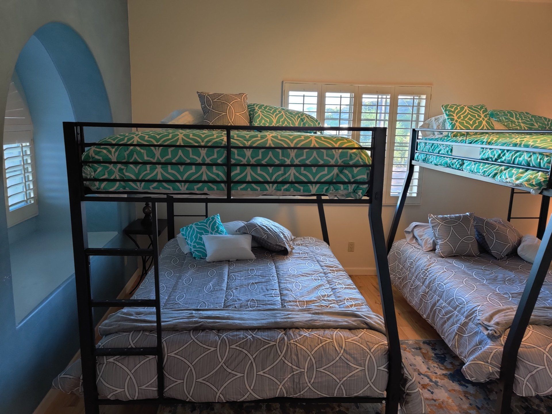 Children’s bedroom with two bunk beds and patterned bedding, blue walls, and a window in back.