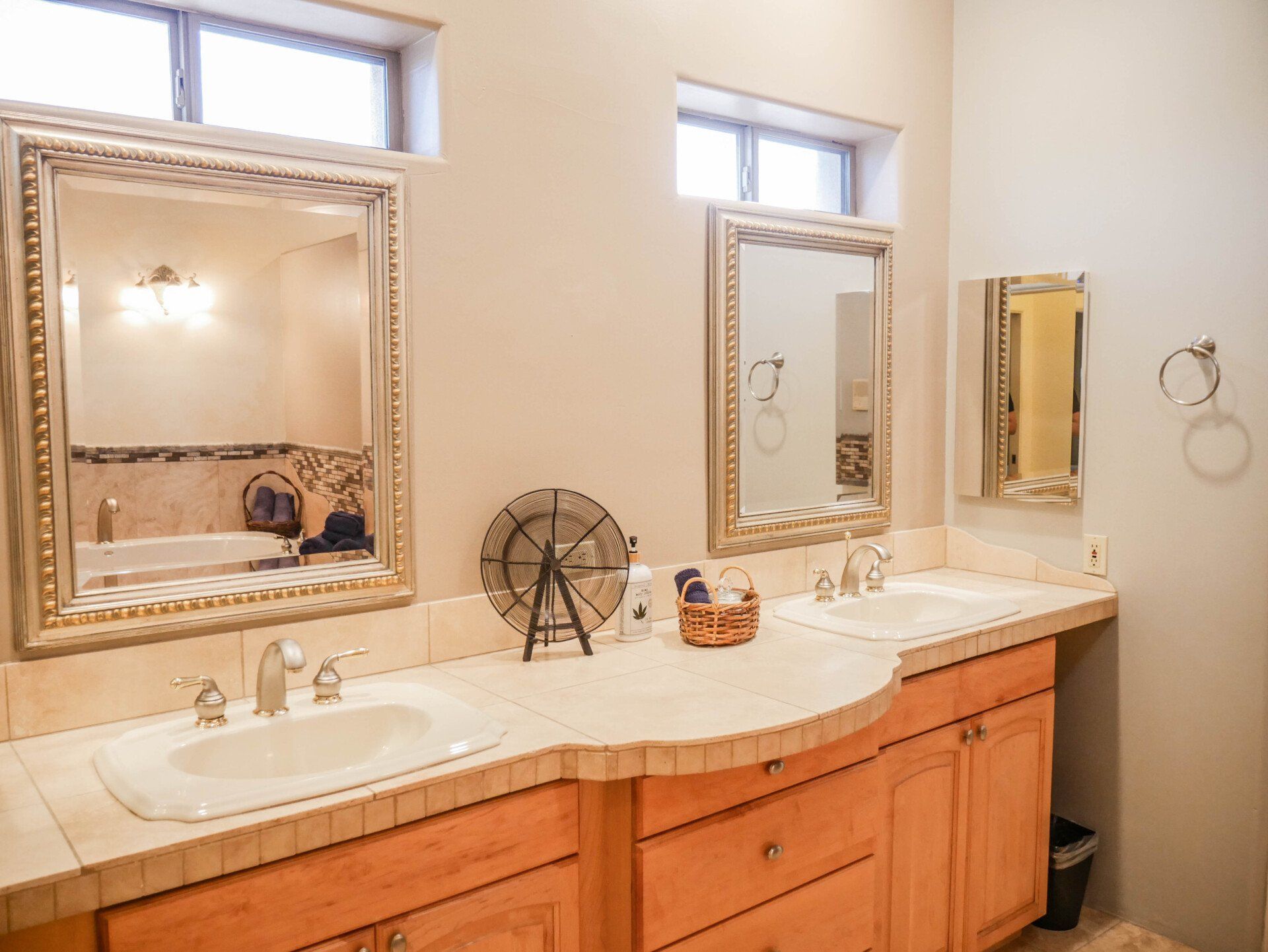 Bright bathroom vanity with two ornate mirrors, double sinks, and a window above the counter
