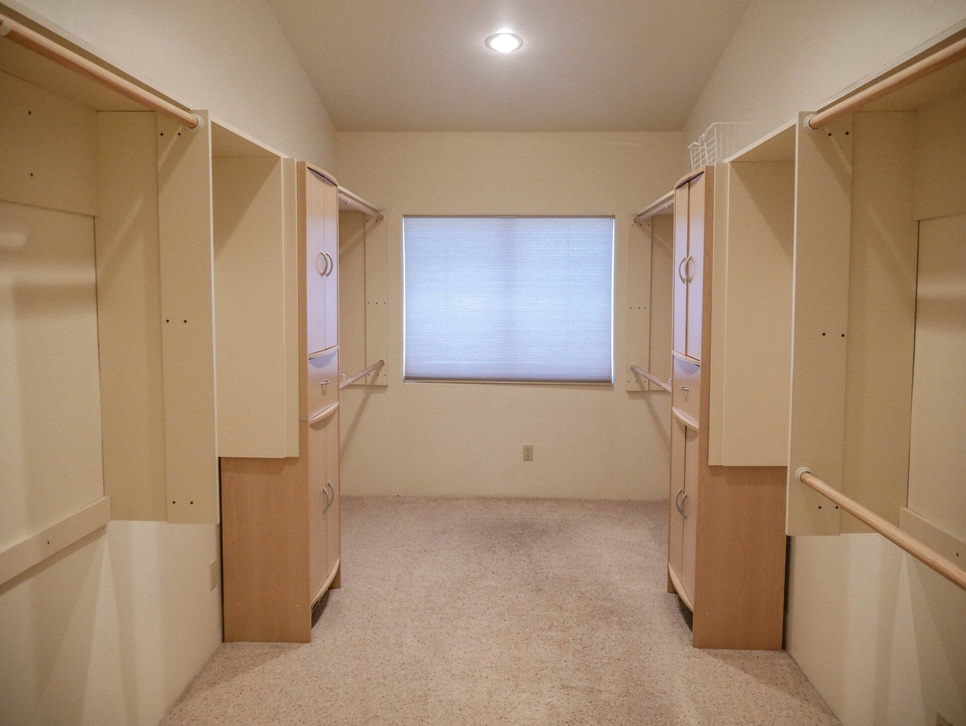 An empty walk in closet with a window and wooden cabinets.